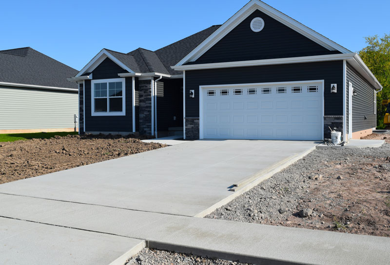 Newly poured concrete driveway in front of a modern residential home, with surrounding construction site