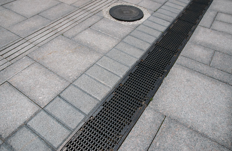 Concrete gutter and drain installation on a paved surface, showing water drainage features and a manhole cover