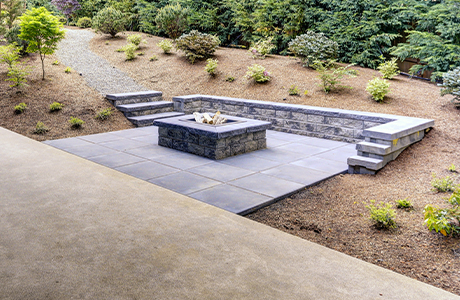 Beautiful modern concrete patio with fire pit, surrounded by landscaped garden with steps leading down to the patio area