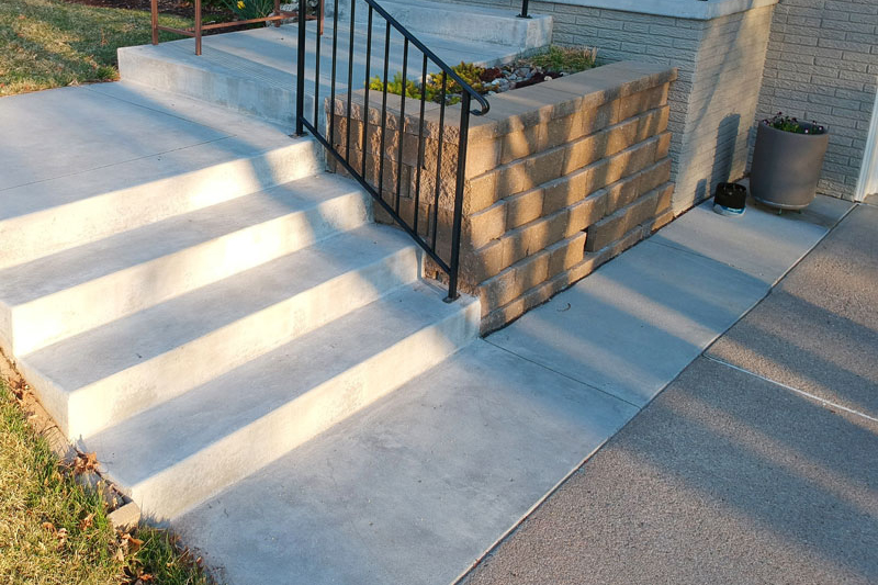 Freshly installed concrete staircase with black metal railing leading to the front porch of a house