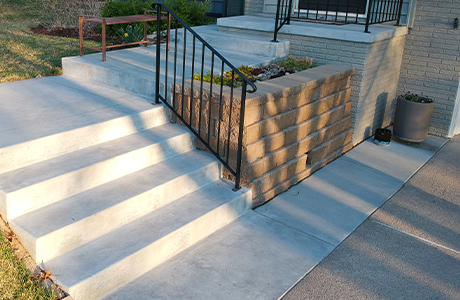 Freshly installed concrete staircase with black metal railing leading to the front porch of a house