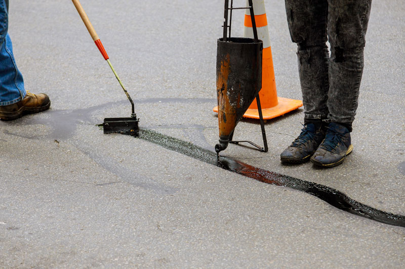 Workers using crack sealing equipment to fill asphalt pavement cracks with sealant for road maintenance