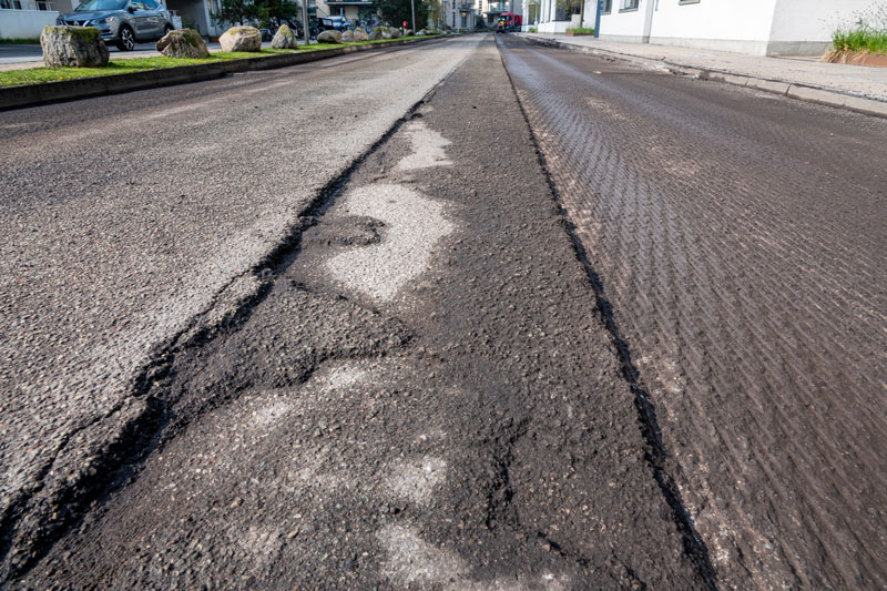 Close-up of a road undergoing asphalt milling services, with visible grooves and removed layers of the old asphalt surface