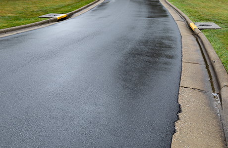 Freshly paved road after asphalt milling to improve drainage, with smooth surface and visible curbside drainage systems