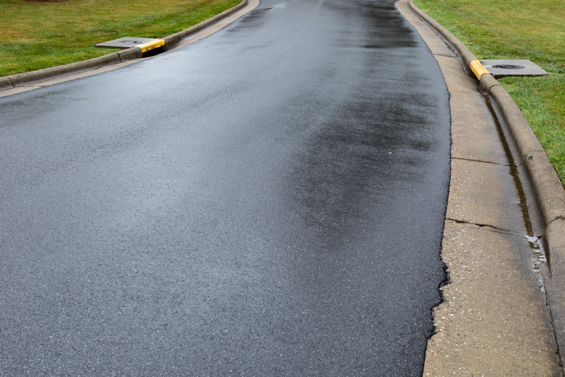 Freshly paved road after asphalt milling to improve drainage, with smooth surface and visible curbside drainage systems