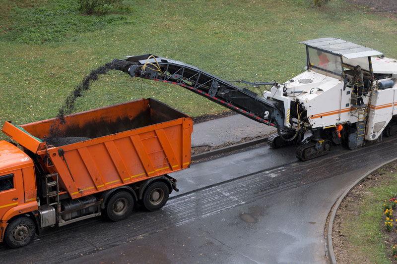 Asphalt milling machine loading removed road materials into a dump truck for recycling during a roadway resurfacing project